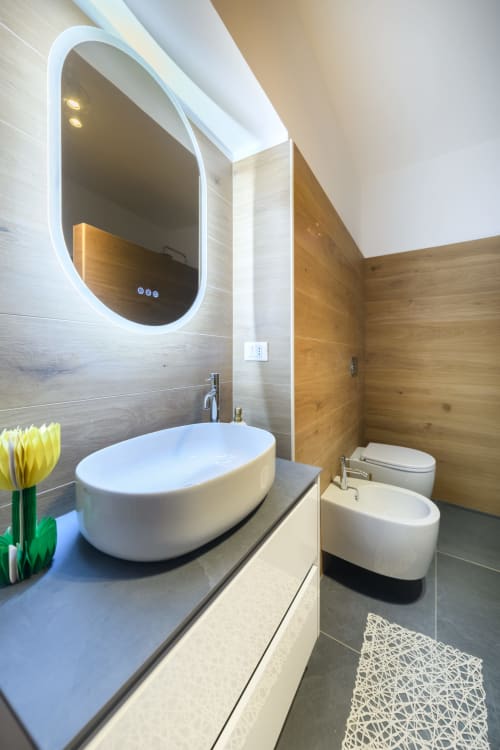 Bagno moderno nell'Almatros Green Apartment a Sulmona con specchio LED ovale, lavabo bianco a terra e dettagli in legno