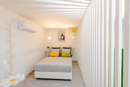 Camera Green dell'hotel Almatros a Sulmona con letto moderno, veneziane bianche verticali e accenti giallo-verde luminosi