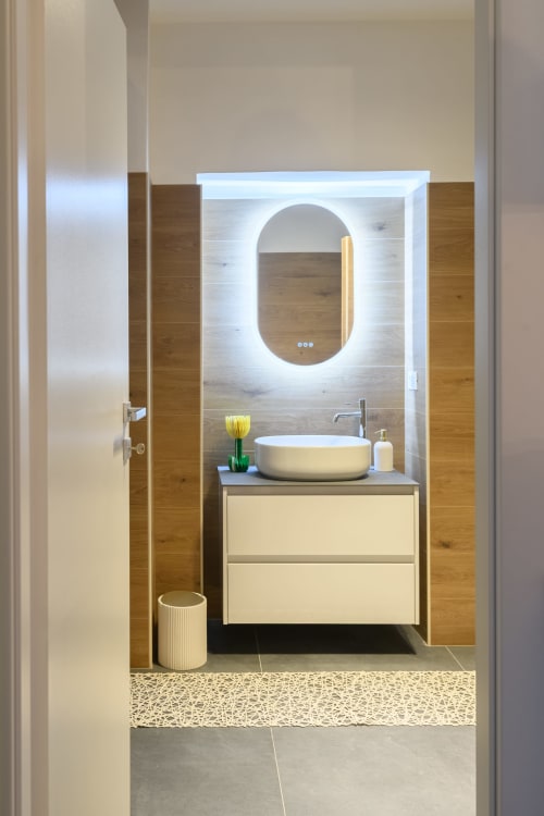Bagno moderno dell'Almatros Green Apartment a Sulmona con specchio ovale illuminato, lavabo bianco e mobile in legno