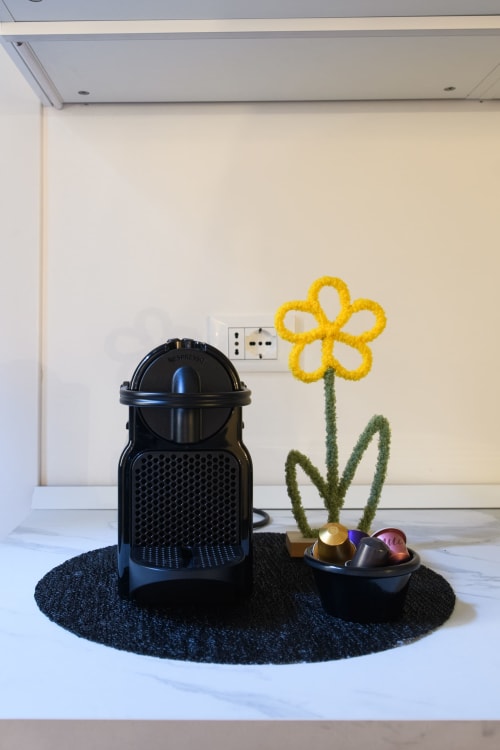Macchina per il caffè nera con decorazione di fiore giallo su tappetino scuro presso l'Almatros Green Apartment a Sulmona