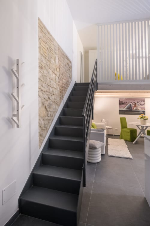 Scala nera nell'Apartment Green dell'hotel Almatros a Sulmona, con parete in pietra e moderna area lounge sottostante