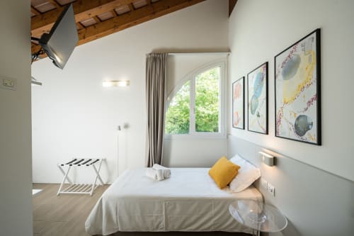 Camera luminosa dell'Hotel Villa Mary con letto bianco, cuscino giallo, finestra con vista giardino e quadro incorniciato a Santa Maria