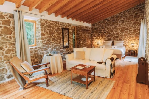 Spacious rustic bedroom at Quinta da Mata de Baixo with stone walls, wooden beams, cream sofa, and garden view in Ferreira do