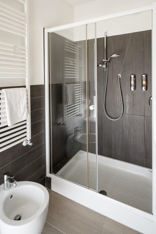 Bagno moderno in Hotel Villa Mary con rivestimenti in legno scuro, box doccia in vetro, lavabo su colonna bianco, scaldasalviette e