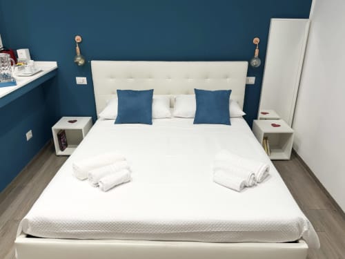 Camera moderna a Harmony House, Bari con letto in tessuto bianco, cuscini blu e parete accent turchese