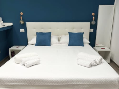 Camera moderna presso Harmony House a Bari con letto imbottito in crema, cuscini blu, pareti turchesi e asciugamani bianchi arrotolati.