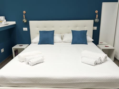 Camera moderna presso Harmony House Bari con letto rivestito in crema, cuscini blu, biancheria bianca e parete accent blu scuro