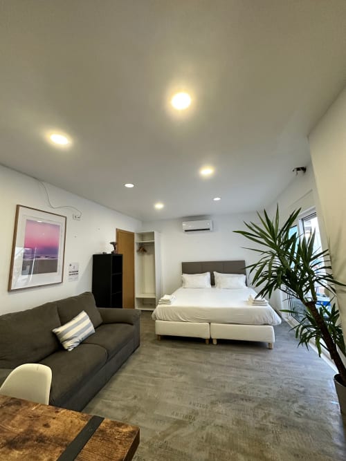 Modern bedroom at Vila Alexandra hostel in Costa da Caparica with bed, sofa, plant, and recessed lighting