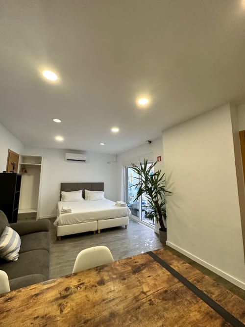 Modern bedroom at Vila Alexandra hostel in Costa da Caparica with white bed, wood table, plant, and recessed lighting