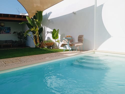 Piscina azul-turquesa na Santa Cruz Historic Guest House em Lagos com espreguiçadeiras, bananeiras e parede branca