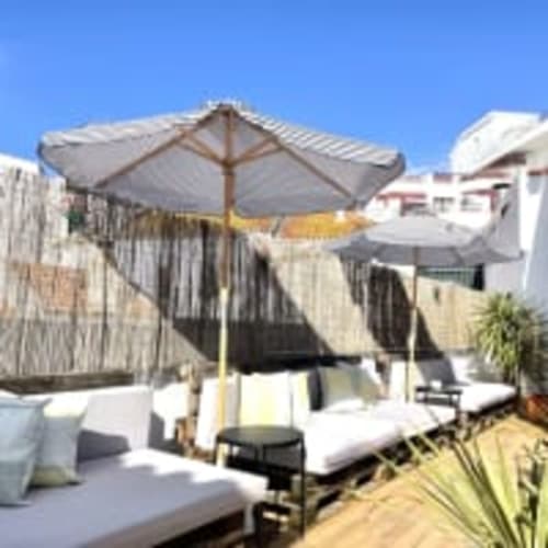 Sunny rooftop terrace at Vila Alexandra hostel in Costa da Caparica with umbrellas, loungers, and white buildings