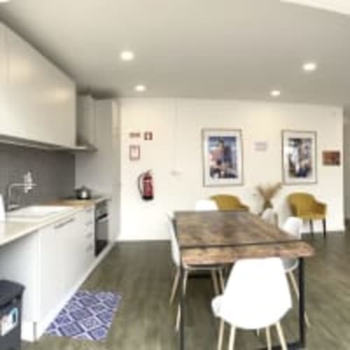Studio at Vila Alexandra hostel in Costa da Caparica featuring modern kitchen, dining table, yellow chairs, and living area