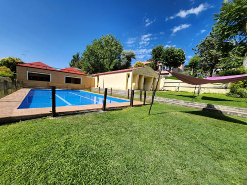 Piscina azul rodeada de césped verde en la casa rural Fuente Vieja de Arbancón, España, con edificios y árboles