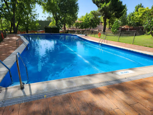 Piscina municipal de aguas cristalinas en el alojamiento rural Fuente Vieja de Arbancón, España, rodeada de árboles y tarimas de madera