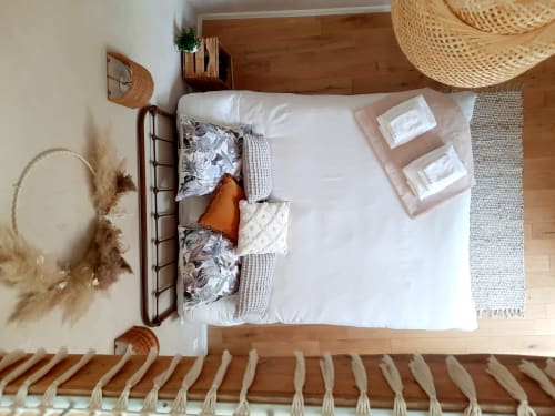 Overhead view of a cozy bedroom at Le Petit Bégou B&B with wooden bed, white linens, decorative pillows, woven hats, and