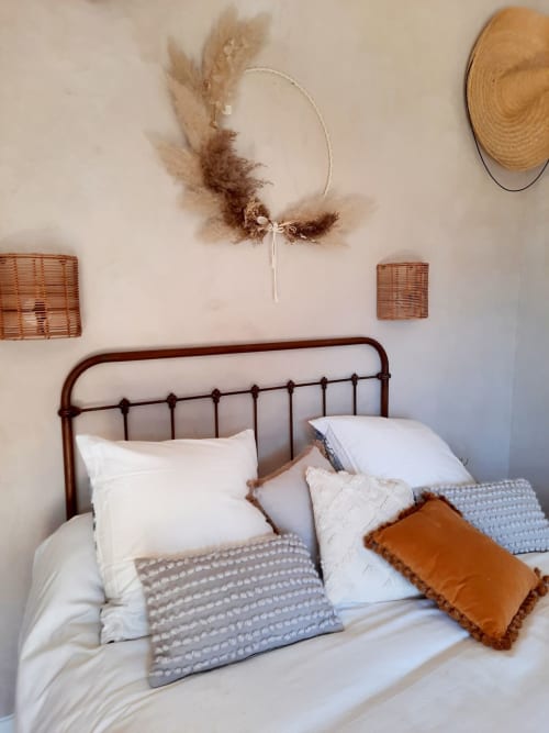 Cozy bedroom at Le Petit Bégou with iron bed, white linens, and rustic pampas grass wall décor in Saint-Auban-d'Oze