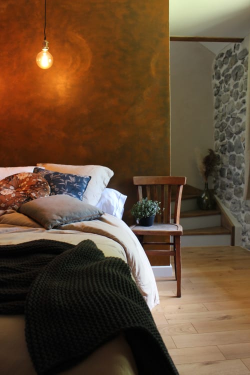 Chambre du Petit Bégou avec mur texturé rouille, suspension luminaire, mobilier bois et vue sur jardin à Saint-Auban-d'Oze