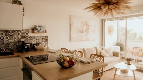 Appartement moderne ouvert chez Sable & Pampas avec îlot de cuisine, canapé crème, chaises tissées et vue panoramique sur la mer