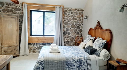 Chambre rustique en pierre au Petit Bégou avec lit en bois, linge blanc et vue sur le jardin