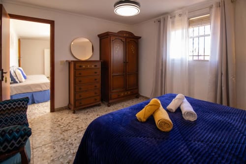 Dormitorio de La Casa de Tita Clota en Setenil de las Bodegas con cama azul, armario de madera y ventanas luminosas