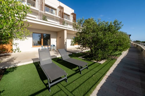 Modern hotel terrace with lounge chairs, sea view, manicured lawn and Mediterranean plants at Hotel Belvedere Resort,