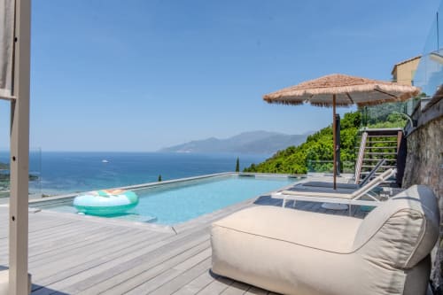Villa Roya infinity pool with sea view overlooking Saint-Florent, lounge chairs and thatched umbrella