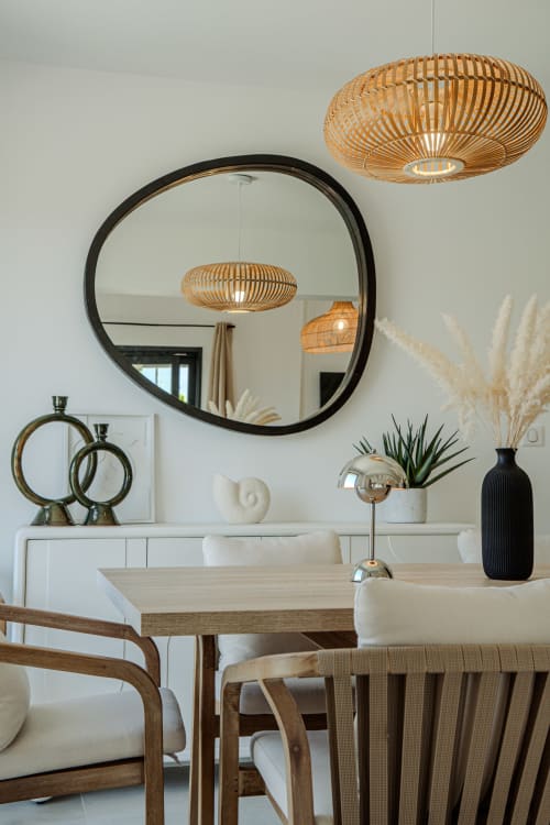 Modern villa dining room at Villa Roya with woven pendant lights, circular black mirror, and wooden furniture in