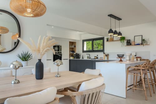 Modern open-plan kitchen and dining area in Villa Roya, Saint-Florent with wooden table, black pendant lights and sea views.