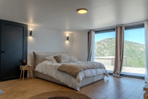Modern villa bedroom at Villa Roya, Saint-Florent with mountain views, neutral bedding, floor-to-ceiling windows, and