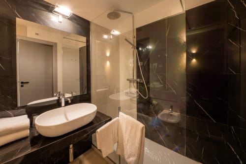 Luxury bathroom in Hotel Belvedere Resort Castellammare del Golfo with black marble, oval sink, and glass shower