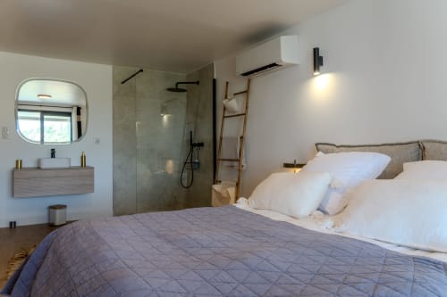 Modern villa bedroom at VILLA ROYA Saint-Florent with bed, ensuite bathroom, shower, and sea view