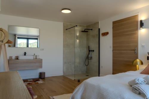 Modern villa bedroom with ensuite bathroom, glass shower, wooden doors, and sea views in Saint-Florent