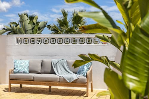 Wooden outdoor sofa with gray cushions and blue pillows on a terrace at Villa Colina, Carvoeiro, surrounded by lush palm
