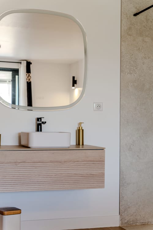 Modern bathroom vanity at Villa Roya in Saint-Florent with round mirror, white sink, and wooden drawer