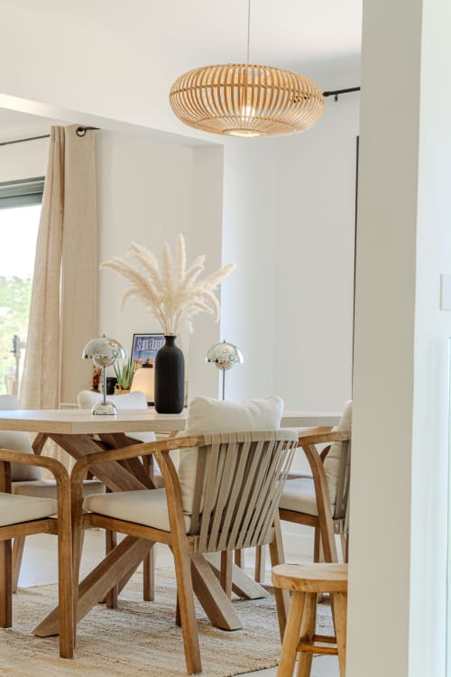 Modern dining room at Villa Roya in Saint-Florent with wooden table, woven pendant light, and sea views through large windows