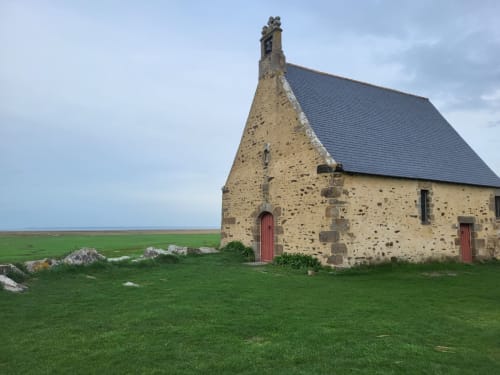 Chapelle historique en pierre aux portes rouges surplombant les champs verdoyants et la mer, Le Clos De La Côte D'émeraude, Bretagne