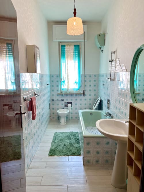 Bagno luminoso nell'appartamento Casa Nicola a San Vito Chietino con piastrelle turchesi, lavabo su colonna, vasca e lampada a sospensione