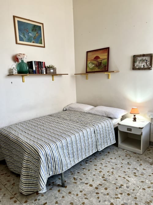 Camera da letto accogliente nell'appartamento Casa Nicola, San Vito Chietino con lenzuola a righe, mensole a parete, lampada comodino e quadro incorniciato