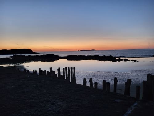 Coucher de soleil sur la côte rocheuse avec poteaux en bois à Saint-Benoît-des-Ondes, Bretagne