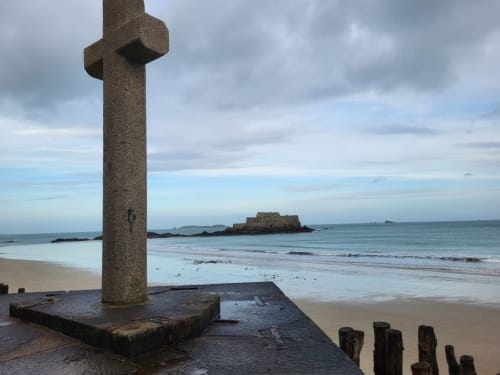 Croix celtique en pierre sur la plage de Saint-Benoît-des-Ondes avec fort et vue sur l'océan, Bretagne France