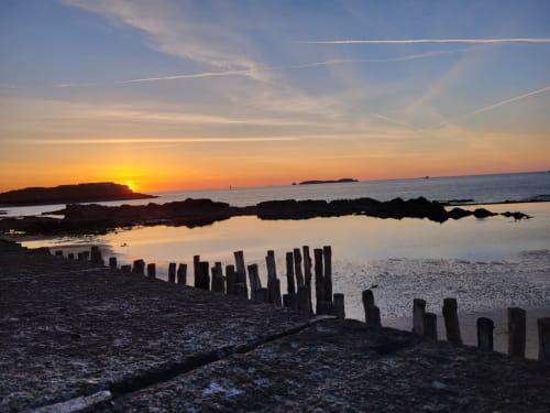 Coucher de soleil sur la plage de la Côte d'Émeraude à Saint-Benoît-des-Ondes avec pieux en bois et bassins de marée