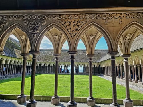Cloître monastique gothique aux colonnes de pierre et fenêtres en arc donnant sur une cour verdoyante à Saint-Benoît-des-Ondes