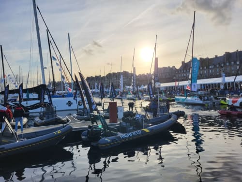 Voiliers et bateaux à moteur amarrés au port de Saint-Benoît-des-Ondes au coucher du soleil, se reflétant dans les eaux calmes avec les bâtiments côtiers