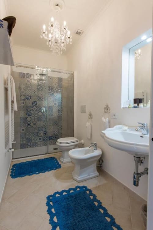 Bagno elegante al Relais Palazzo Cacace con doccia walk-in, pavimenti in marmo, lampadario di cristallo e vasca blu decorativa