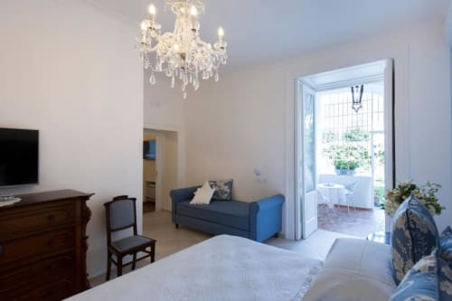 Lussuosa camera al Relais Palazzo Cacace con divano blu, lampadario e terrazza con vista sul giardino a Meta di Sorrento