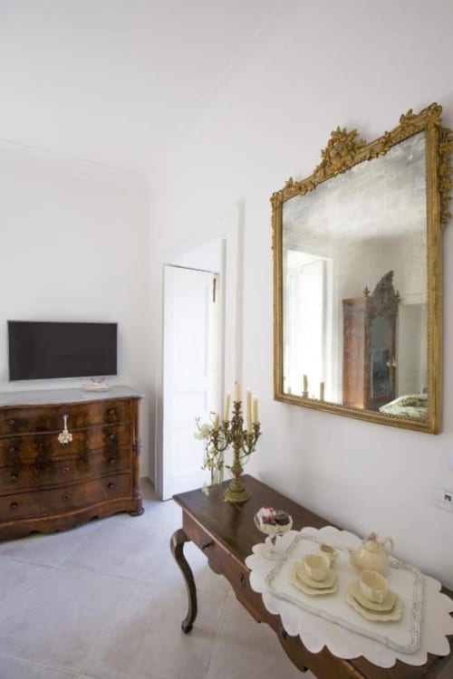 Camera elegante con specchio dorato ornamentale, mobili in legno antico e pavimentazione in marmo presso Relais Palazzo Cacace a Meta di