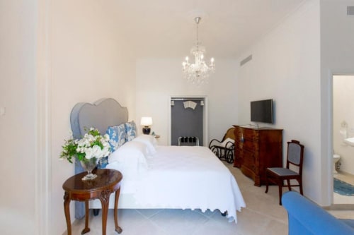Elegante camera Relais Palazzo Cacace con letto bianco, lampadario e vista giardino