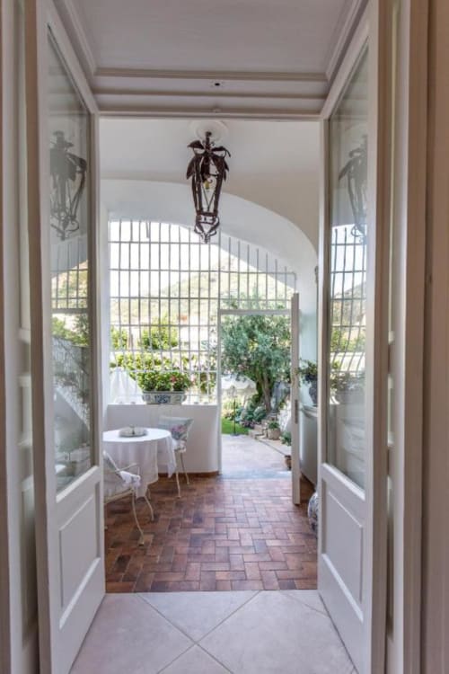 Elegante corridoio del Relais Palazzo Cacace che si apre su una terrazza giardino con tavolo bianco e vista sul Mediterraneo
