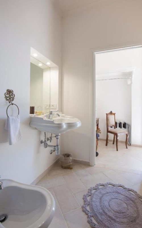 Bagno moderno nella suite Anthea di Relais Palazzo Cacace a Meta di Sorrento, con lavabo su piedistallo, specchio illuminato e rivestimenti in piastrelle