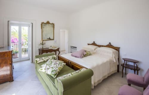 Trilocale Bouganvillea al Relais Palazzo Cacace a Meta di Sorrento con letto in legno, divano verde, balcone e vista giardino